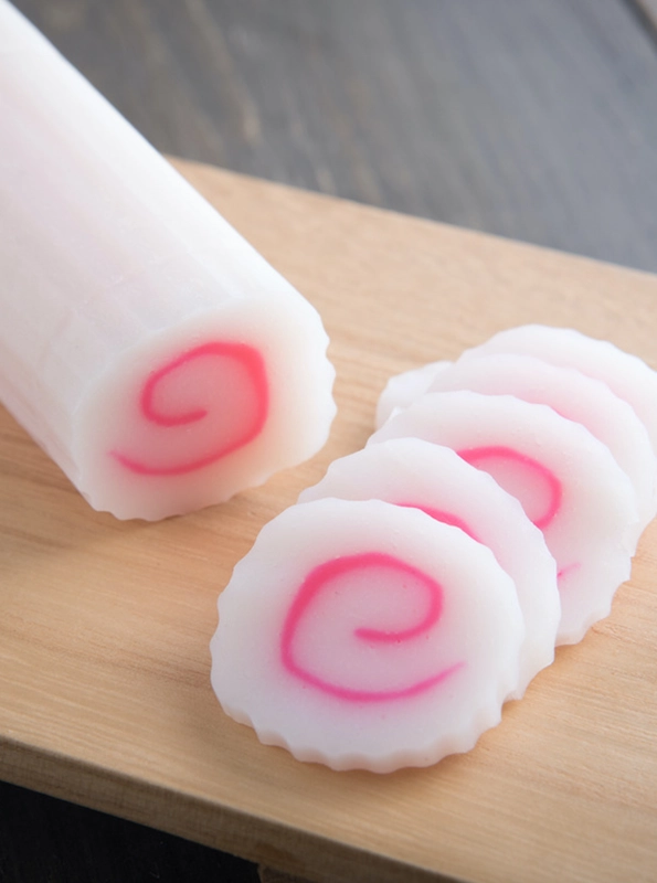Στρογγυλές φέτες ιαπωνικού narutomaki, λευκό κέικ ψαριού με ροζ σπείρα στο κέντρο, τοποθετημένες σε ξύλινη επιφάνεια κοπής.
