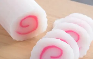 Στρογγυλές φέτες ιαπωνικού narutomaki, λευκό κέικ ψαριού με ροζ σπείρα στο κέντρο, τοποθετημένες σε ξύλινη επιφάνεια κοπής.