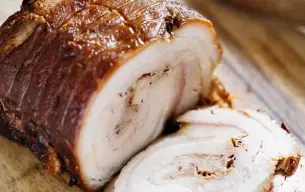 Ρολό από σιγομαγειρεμένη χοιρινή κοιλιά Chashu, κομμένο σε λεπτές φέτες, τοποθετημένο σε ξύλινη επιφάνεια κοπής, έτοιμο για χρήση ως επικάλυψη σε ramen.