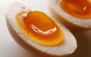 Κοντινό πλάνο δύο μισών αυγών ράμεν (ajitsuke tamago) με μελάτο, λαμπερό κρόκο πάνω σε λευκή επιφάνεια.